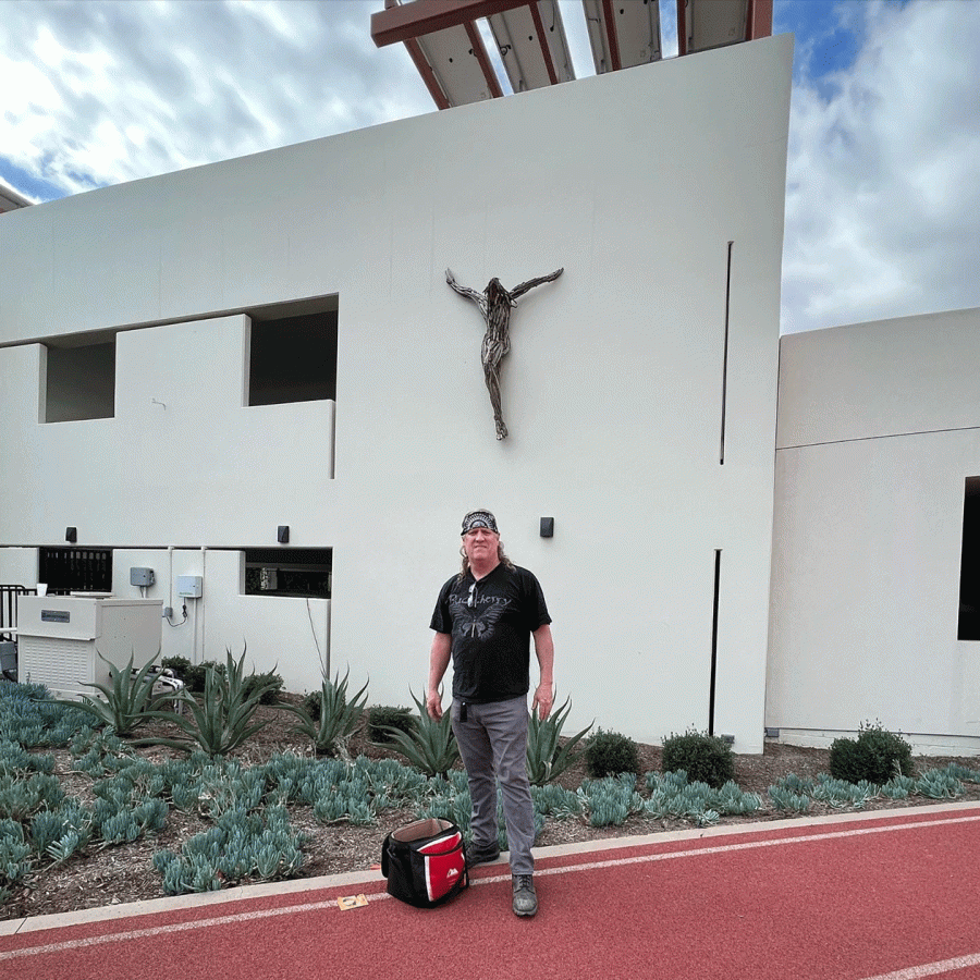 Mike Amato stands in front of the driftwood crucifix on the Arons Family Parking Plaza.