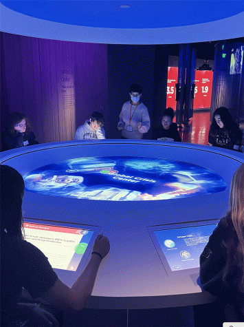 A group of students sitting at a table with interactive screens to learn about crises around the world at the Social Lab.