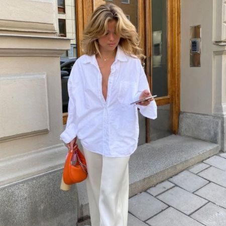 Matilda Djerf wears a white button down and trousers with a bright orange baguette bag; the epitome of the Eurosummer trend.